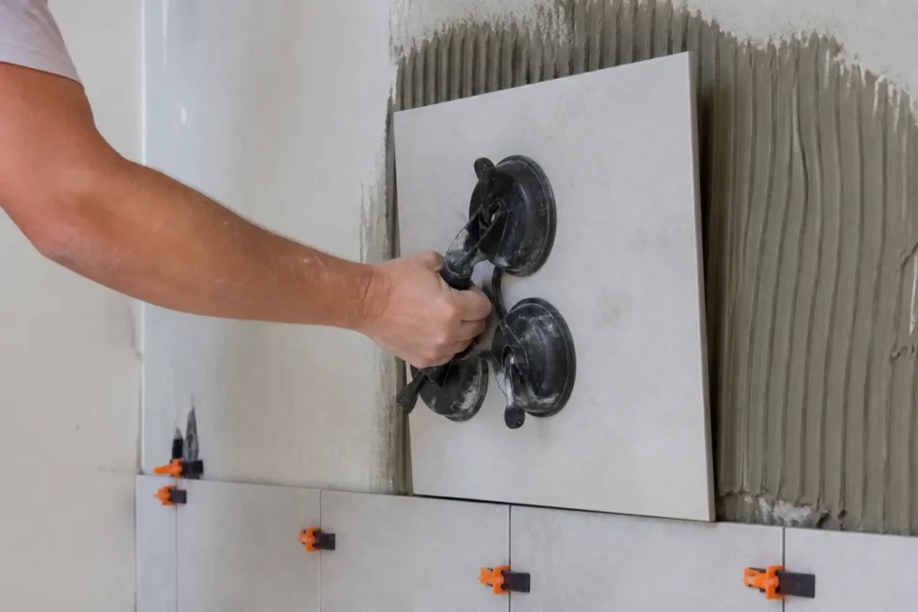 Pose d'un carreau de grès cérame sur un mur, colle peignée au peigne cranté et ventouses de maintien