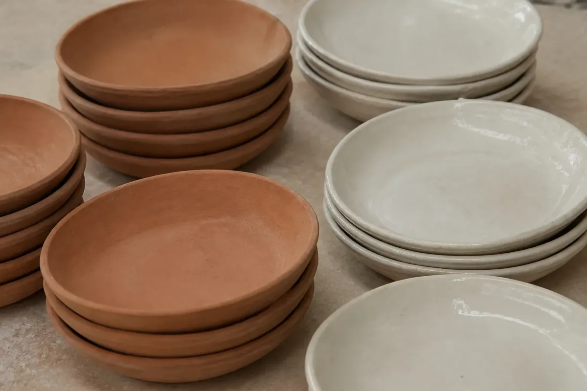 Plats et assiettes en terre cuite crue posés à côté de pièces recouvertes d'un émail blanc brillant.